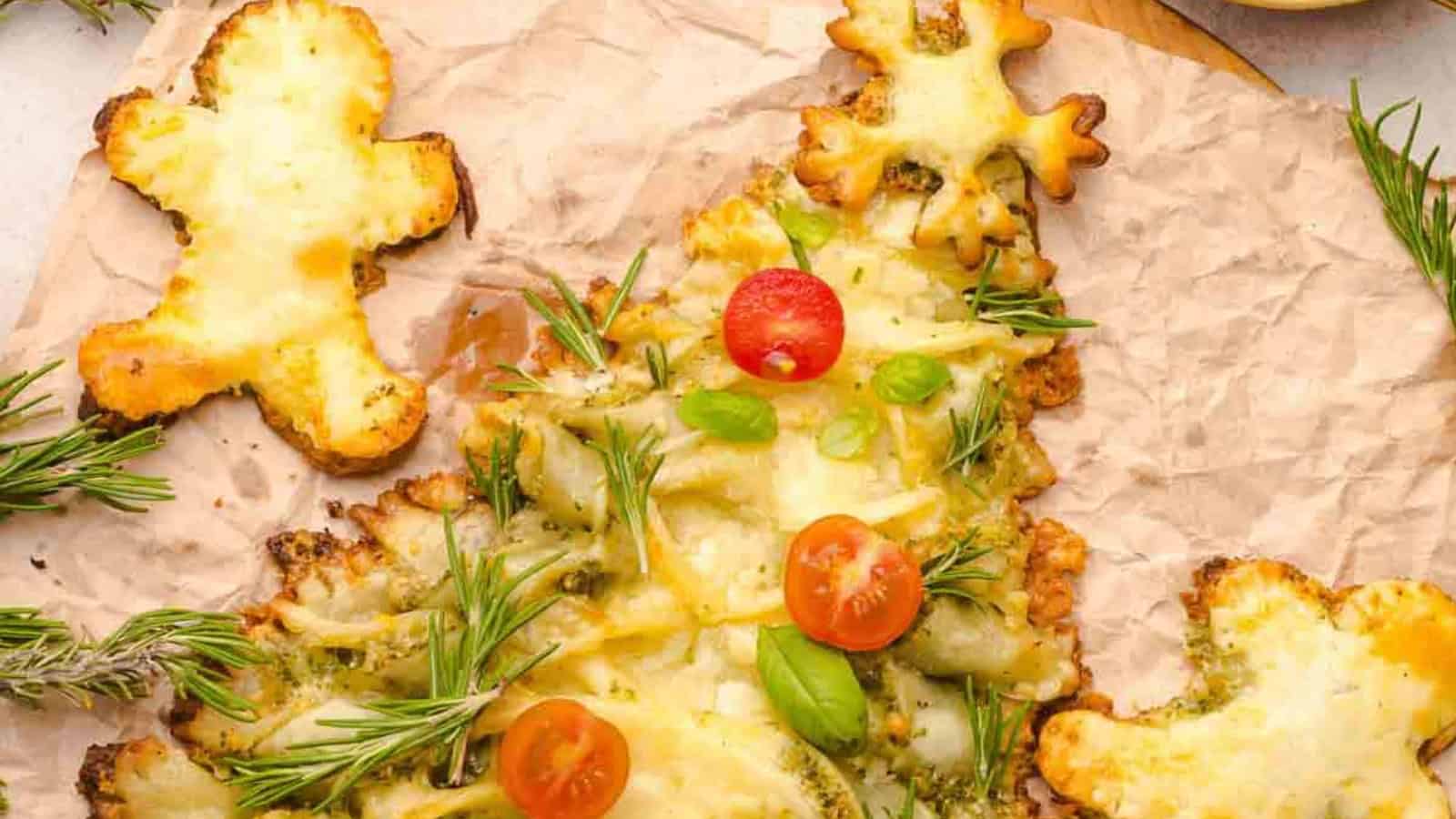 Christmas tree-shaped cheesy bread with cherry tomatoes and herbs, surrounded by star and gingerbread shapes.