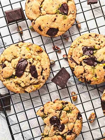 Chocolate chunk cookies cooling on a wire rack, with a bowl of green pistachio spread on the side.