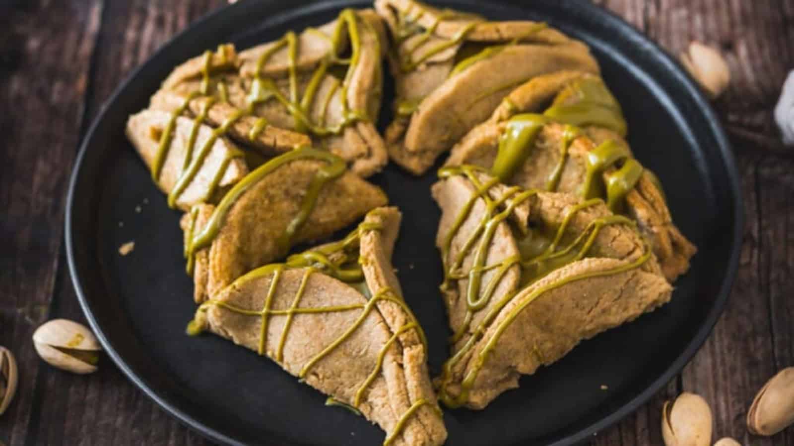 Six pistachio cookies drizzled with green icing arranged in a circle on a black plate.