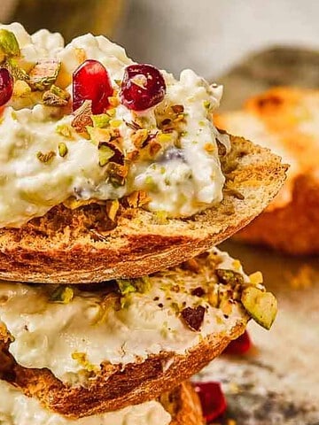 Toasted bread slices topped with creamy cheese, pomegranate seeds, and chopped pistachios.