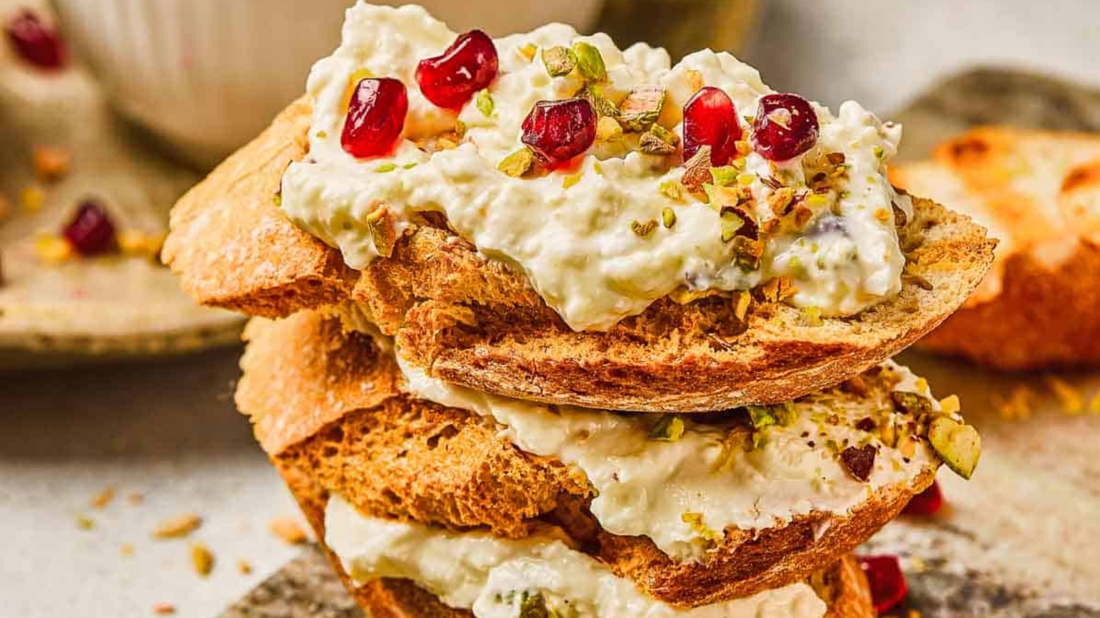 Toasted bread slices topped with creamy cheese, pomegranate seeds, and chopped pistachios.