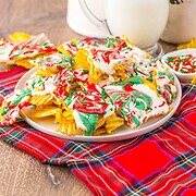 Plate of potato chips drizzled with red, white, and green chocolate—like a festive Christmas Crack recipe—sits next to a glass of milk on a plaid cloth.