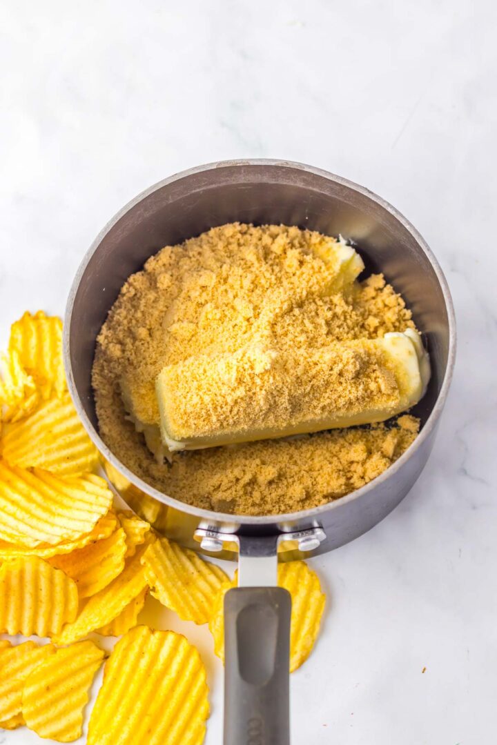 A saucepan with butter and brown sugar, next to ridged potato chips on a white surface&mdash;perfect for making a festive Christmas Crack recipe.
