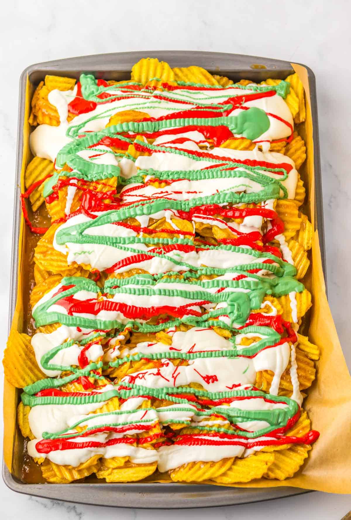 Wavy potato chips are topped with white, red, and green sauces on a rectangular baking sheet&mdash;a festive recipe perfect for your next holiday party.