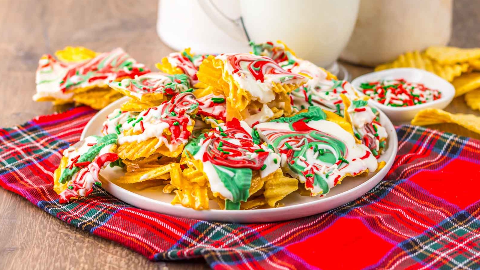 Wavy chips coated in white chocolate with red and green swirls on a plate, on a plaid cloth.