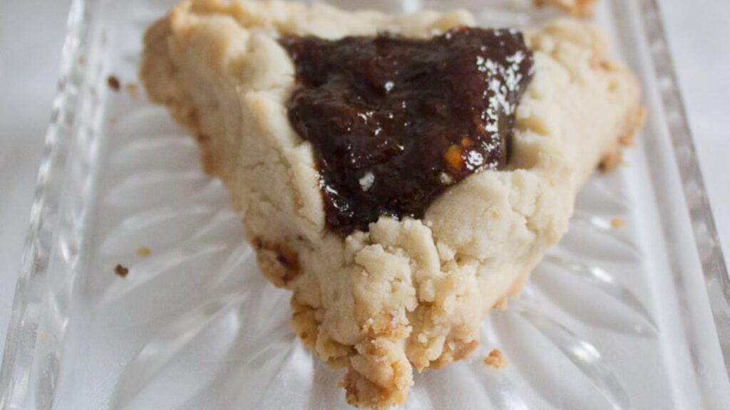 A triangular pastry with crumbly edges and a dark fruit filling, served on a clear glass dish.