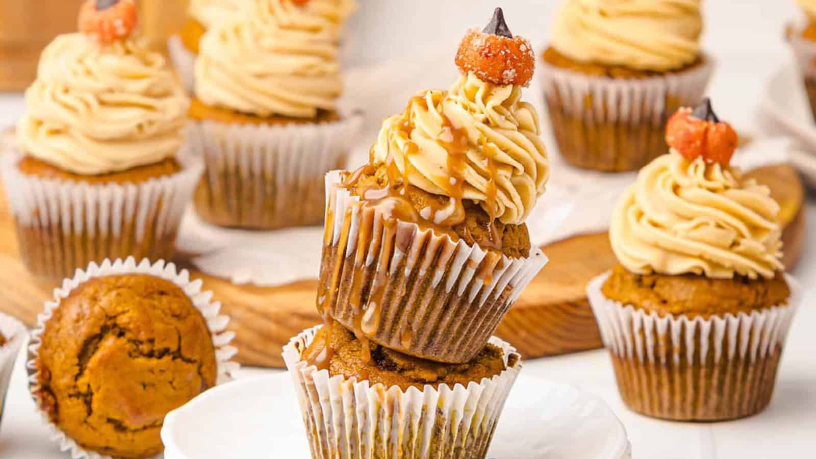 Cupcakes with swirled frosting and caramel drizzle, stacked on a white plate, with more cupcakes in the background.