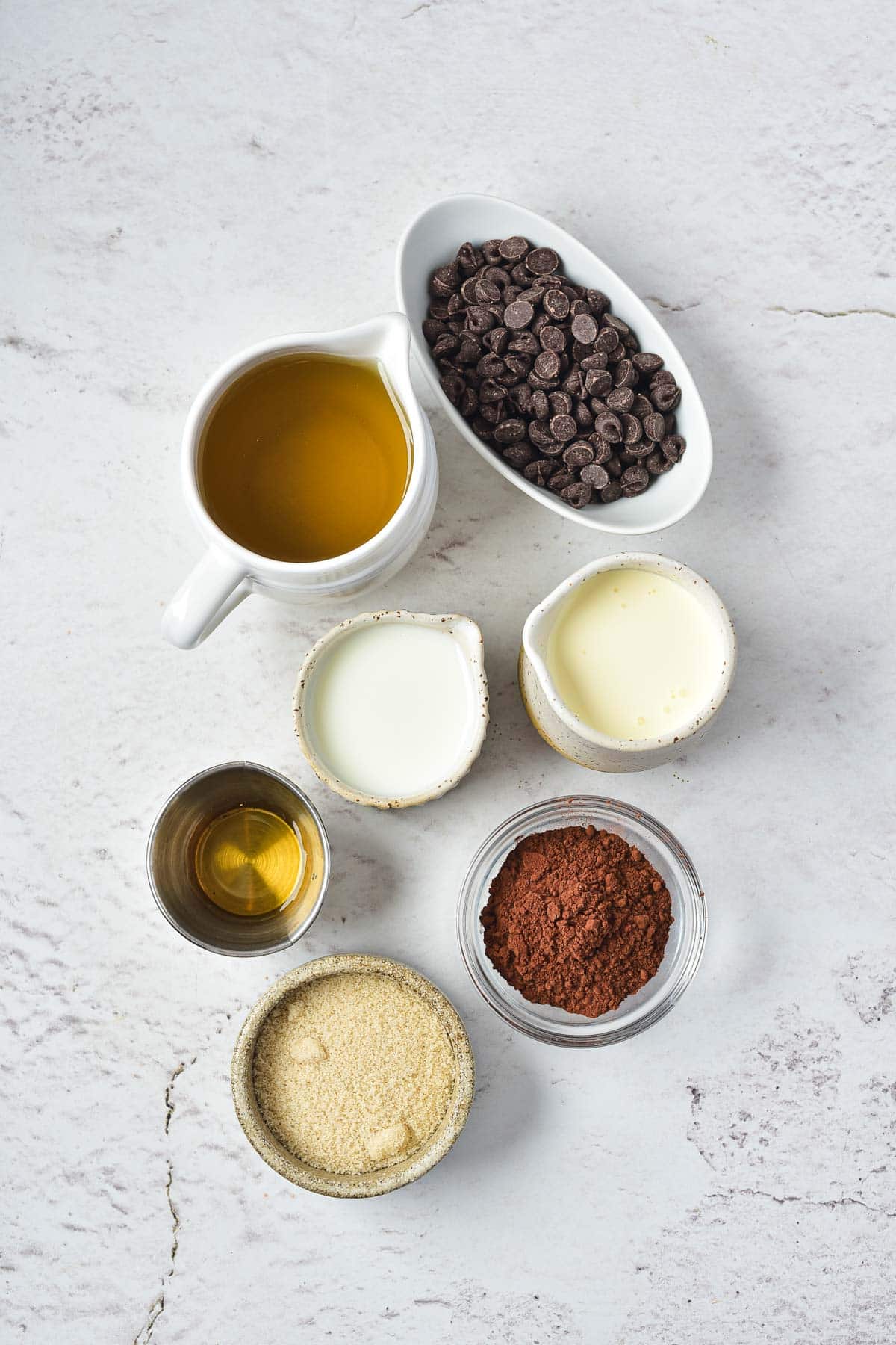 Seven small bowls and pitchers containing chocolate chips, oil, cocoa powder, sugar, milk, cream, and vanilla extract for making delicious Instant Pot Hot Chocolate.