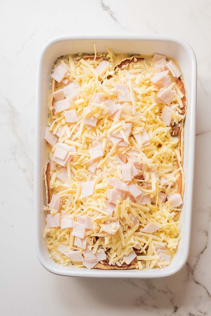 White baking dish with layered bread, shredded cheese, and diced turkey on a marble surface&mdash;perfect for a hearty Breakfast Casserole Recipe.