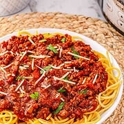 Plate of Spaghetti Bolognese topped with savory meat sauce, garnished with parsley and grated cheese, served on a woven placemat.