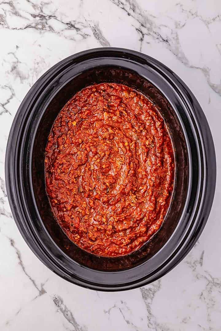 Overhead view of rich tomato meat sauce in a black Crockpot on a marble countertop, perfect for Spaghetti Bolognese.