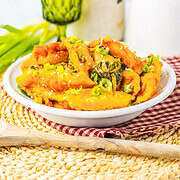 A bowl of tteokbokki garnished with green onions and sesame seeds sits on a woven mat, capturing the cozy kitchen vibe that's been trending on TikTok alongside favorites like the Viral Dumpling Bake.