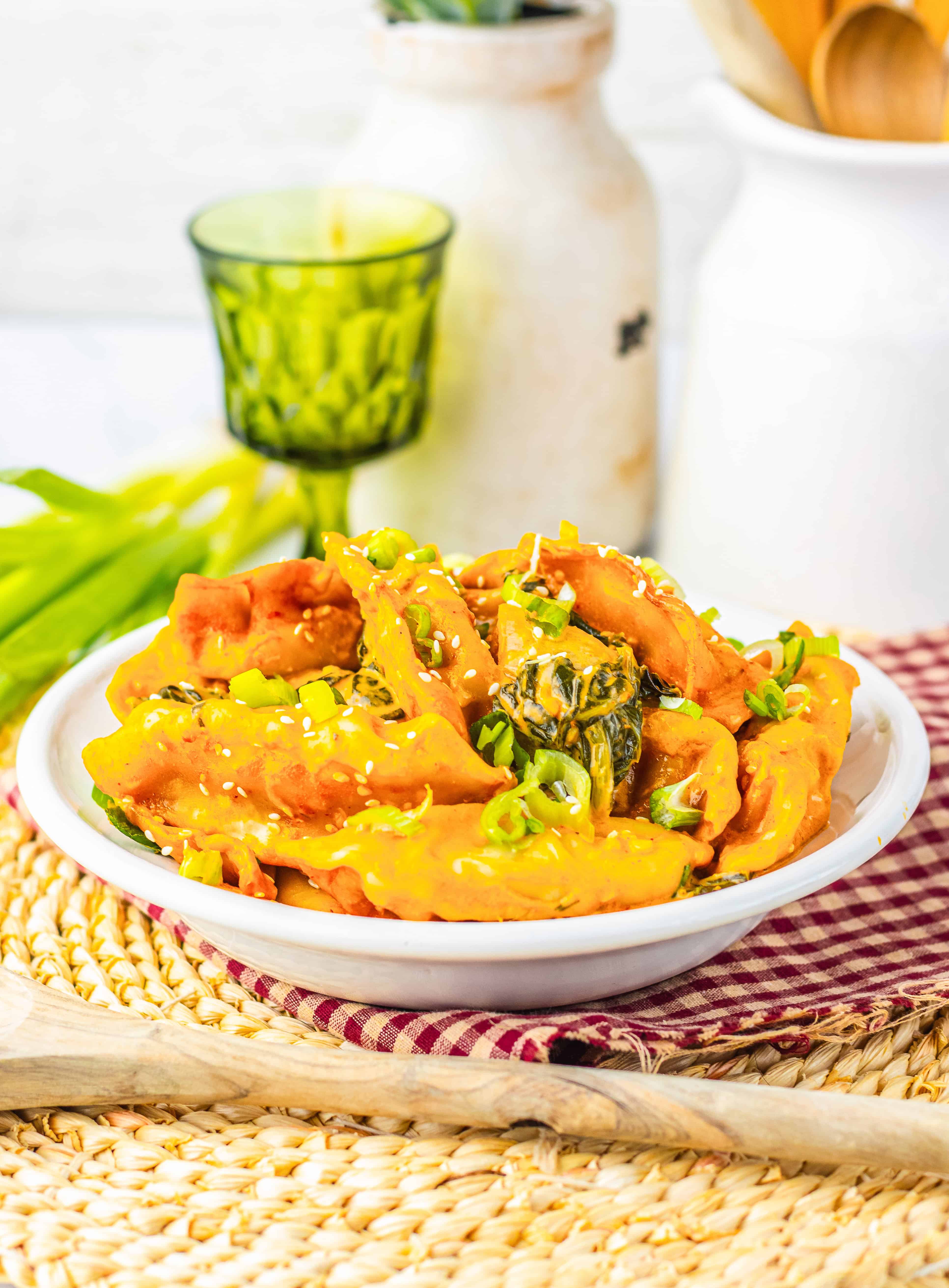 A bowl of tteokbokki garnished with green onions and sesame seeds sits on a woven mat, capturing the cozy kitchen vibe that's been trending on TikTok alongside favorites like the Viral Dumpling Bake.