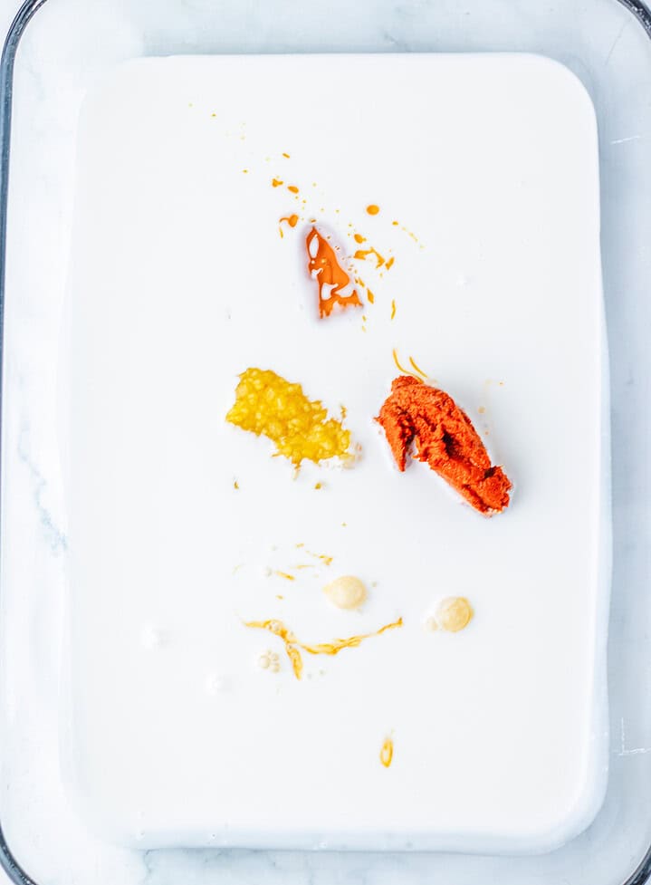 A white liquid in a glass dish with dollops of red, yellow, and beige pastes on top—this tempting setup is perfect for recreating the viral Dumpling Bake trend seen everywhere on TikTok.