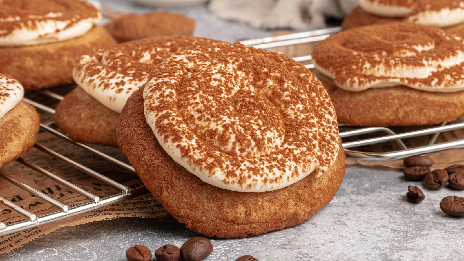 Close-up of cookies topped with swirled cream and cocoa powder, cooling on a wire rack.