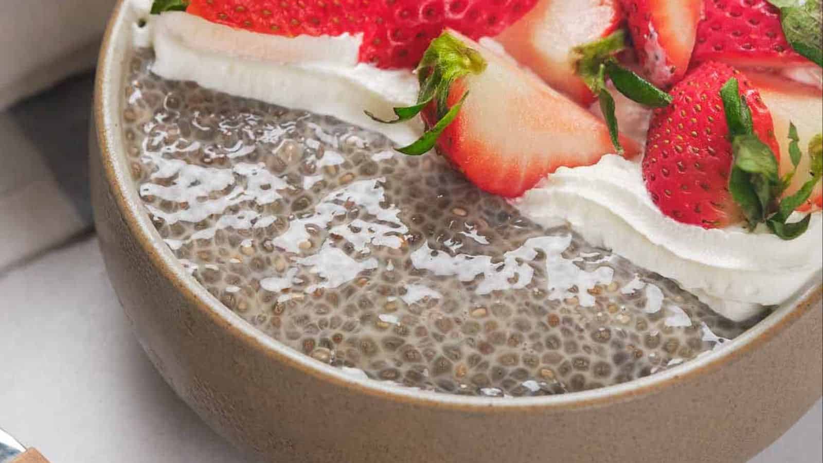 A bowl of chia pudding topped with sliced strawberries and a dollop of whipped cream, with a spoon lifting a portion.