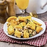 A plate of gnocchi with creamy sauce and herbs, served with orange slices on a red checkered napkin.