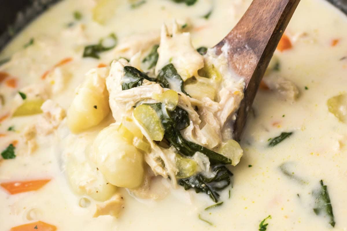 Close-up of creamy Chicken Gnocchi Soup with vegetables and spinach, gently stirred with a wooden spoon&mdash;perfect for cozy nights or an easy slow cooker meal.