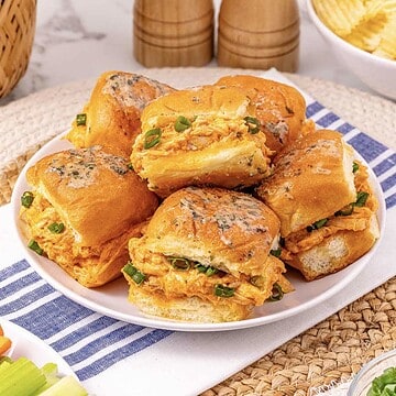 A plate of Easy Chicken Sliders filled with shredded chicken and green onions is served on a blue-striped cloth.