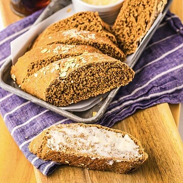 Sliced Cheesecake Factory Bread with butter on a piece, served on a tray with a purple-striped cloth underneath.
