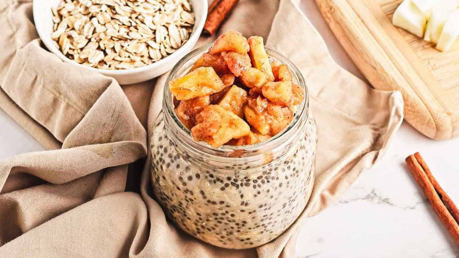 A jar of chia seed pudding topped with caramelized apple pieces, with apples in the background.