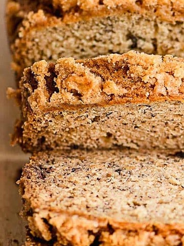 Sliced banana bread with a crumbly topping on a wooden cutting board.