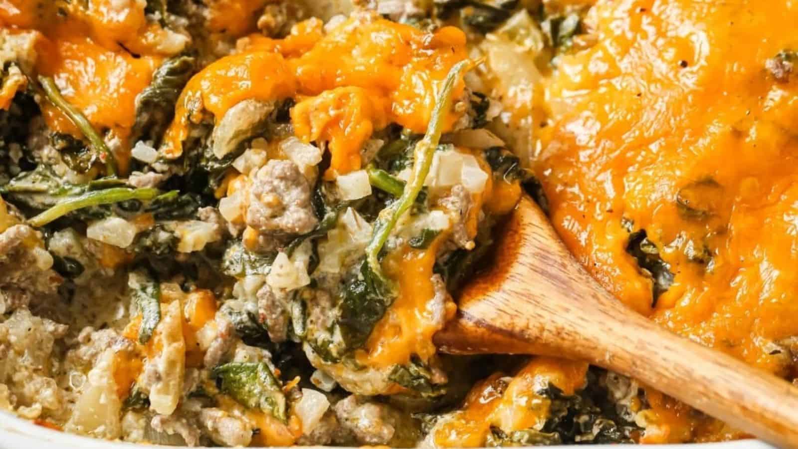 Cheesy beef casserole with cauliflower rice and spinach being spooned out of a baking dish.