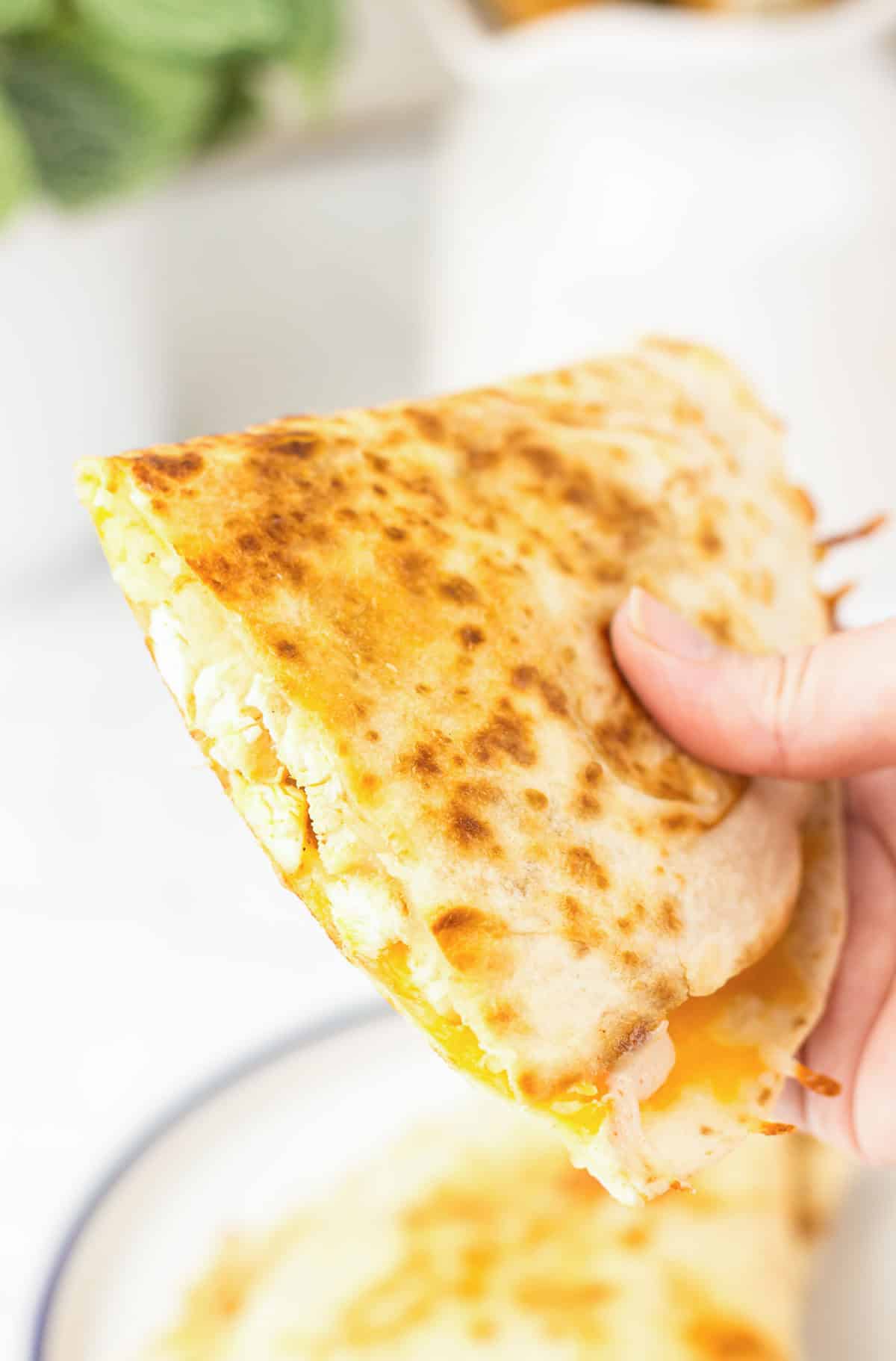 A hand holds a golden, cheesy Copycat Taco Bell Chicken Quesadilla with perfectly melted cheese visible between the toasted tortillas.
