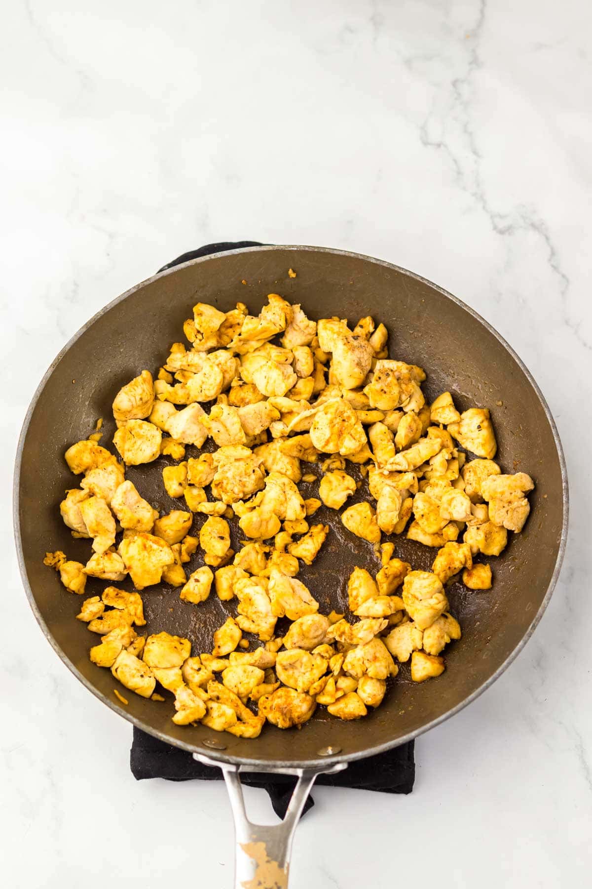 Cooked, seasoned pieces of chicken in a skillet on a light marble countertop—perfect for making a Taco Bell Chicken Quesadilla copycat at home.