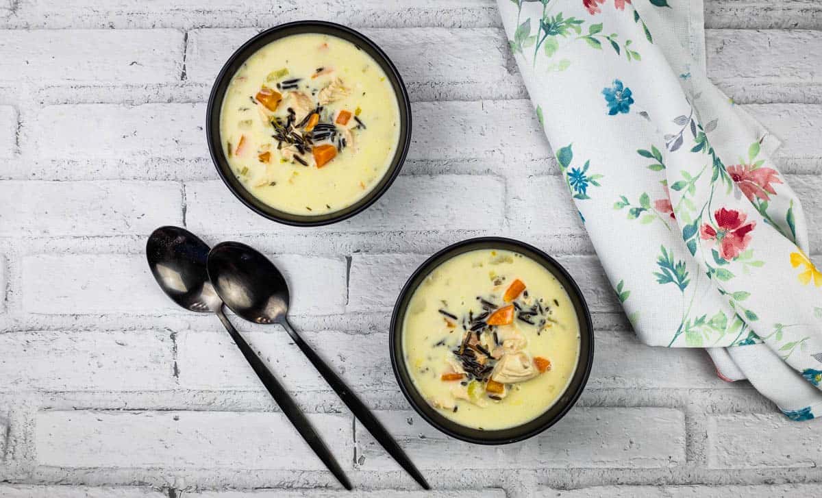 Two bowls of creamy chicken & wild rice soup on a wooden table.