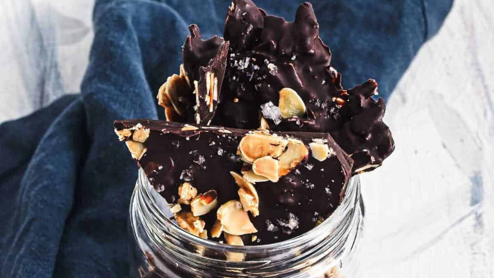 A stack of dark chocolate bark with almonds and sea salt on a marble surface.