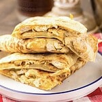 Three sliced Copycat Chicken Quesadillas, inspired by Taco Bell, stacked on a white plate with a red checkered napkin beside them.