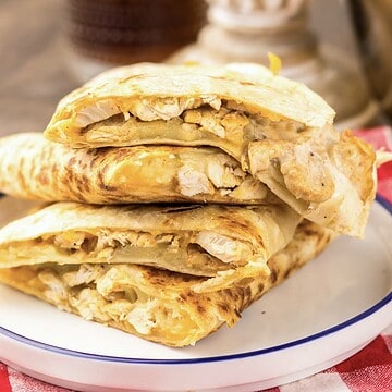Three sliced Copycat Chicken Quesadillas, inspired by Taco Bell, stacked on a white plate with a red checkered napkin beside them.