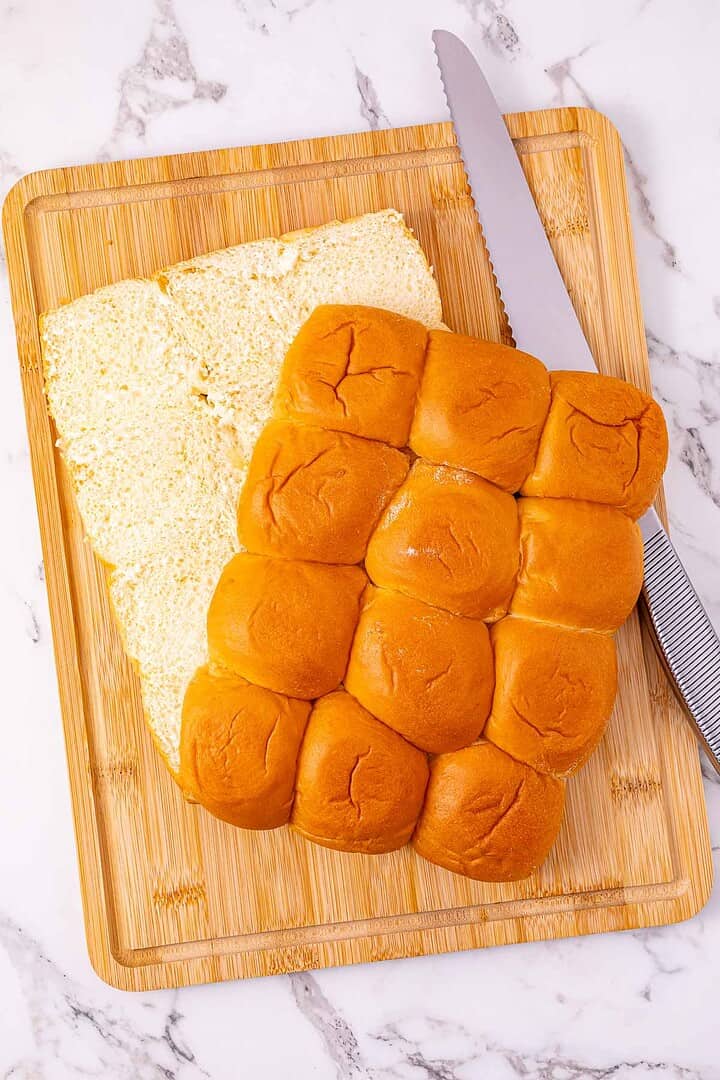 A sliced slab of Easy Chicken Sliders on a wooden cutting board with a serrated knife beside them.