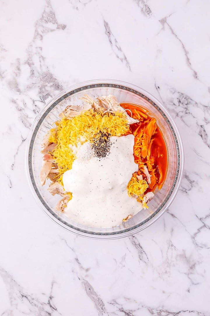 Clear glass bowl with shredded chicken, cheese, buffalo sauce, and ranch dressing on a marble surface&mdash;perfect for making flavorful Buffalo chicken sliders or easy sliders at your next gathering.