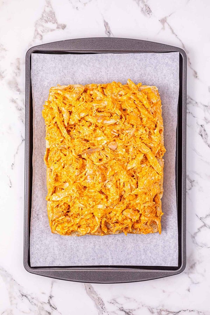 Rectangular layer of shredded Buffalo Chicken mixture on parchment paper in a baking tray, perfect for making Easy Chicken Sliders.