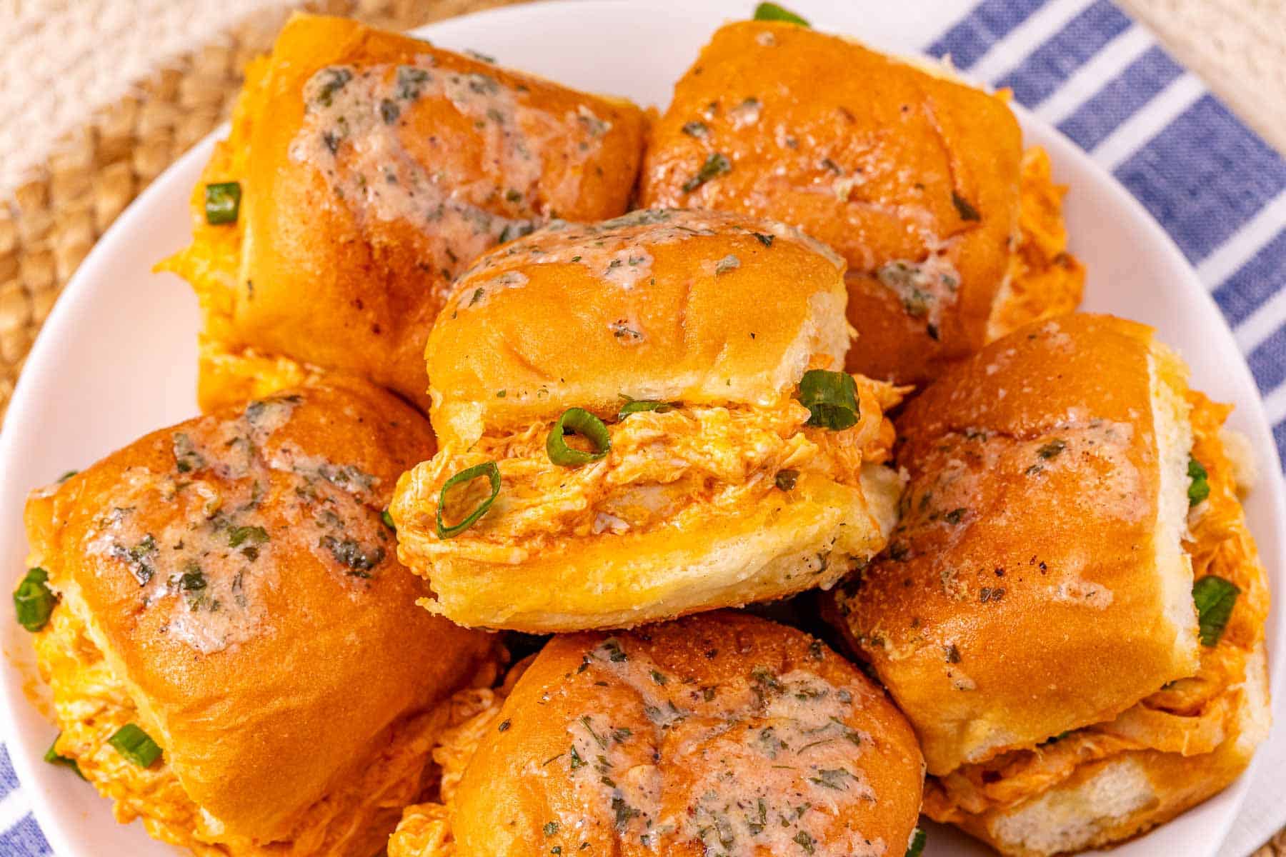A plate of easy Buffalo Chicken Sliders topped with herbs and cut green onions sits on a blue striped towel.