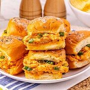 Buffalo Chicken Sliders topped with green onions are served on a plate, with chips and pepper mills in the background—perfect for an easy chicken sliders party snack.