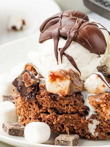 A slice of chocolate dessert topped with ice cream, mini marshmallows, and a drizzle of chocolate sauce.