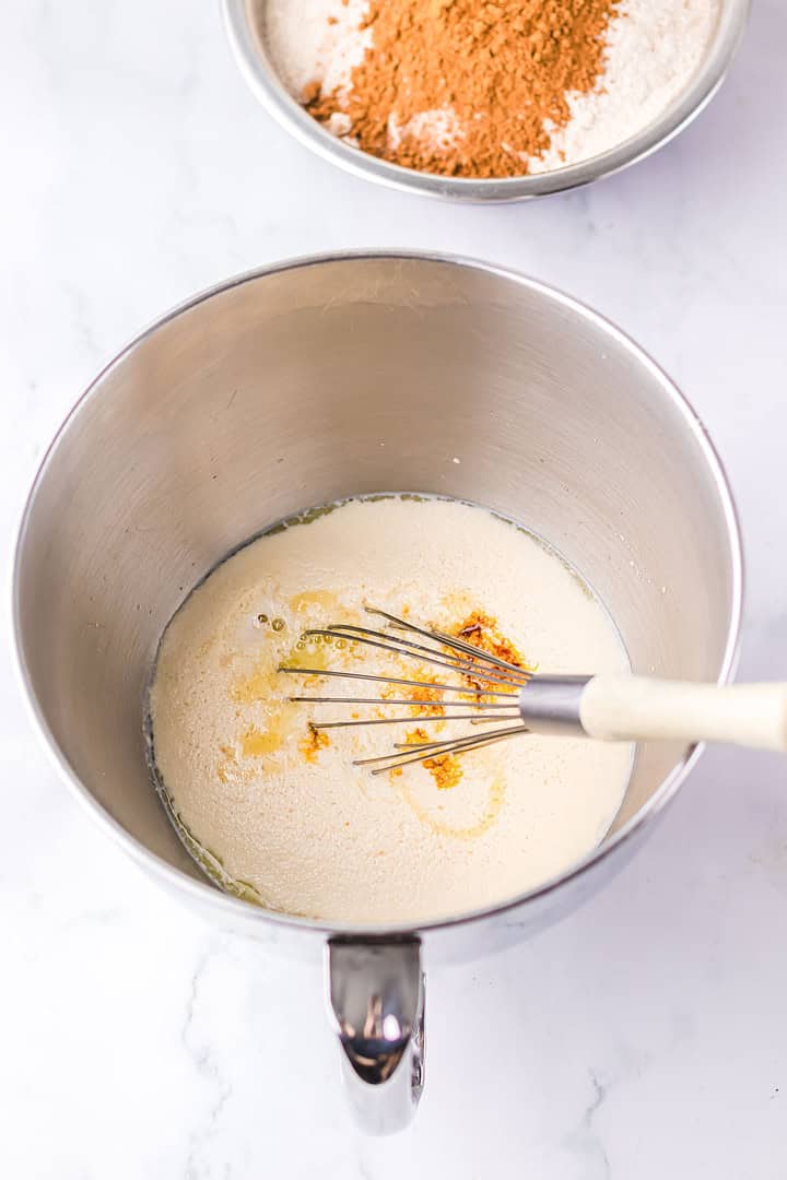 A whisk in a mixing bowl with wet ingredients; a bowl of dry ingredients for Brown Bread is in the background, reminiscent of the popular Cheesecake Factory recipe.