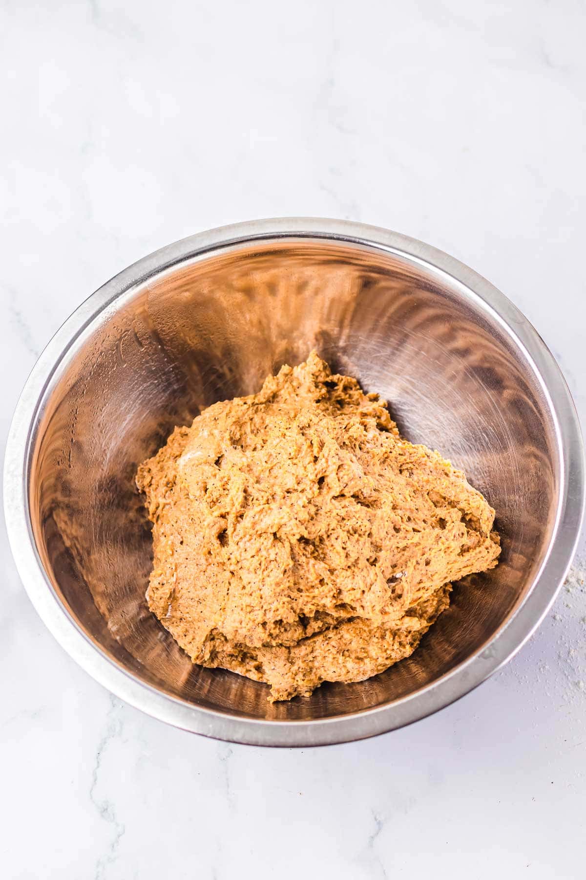 A stainless steel bowl filled with raw cookie dough sits on a white marble surface, reminiscent of the warm, fresh-baked delights from the Cheesecake Factory.