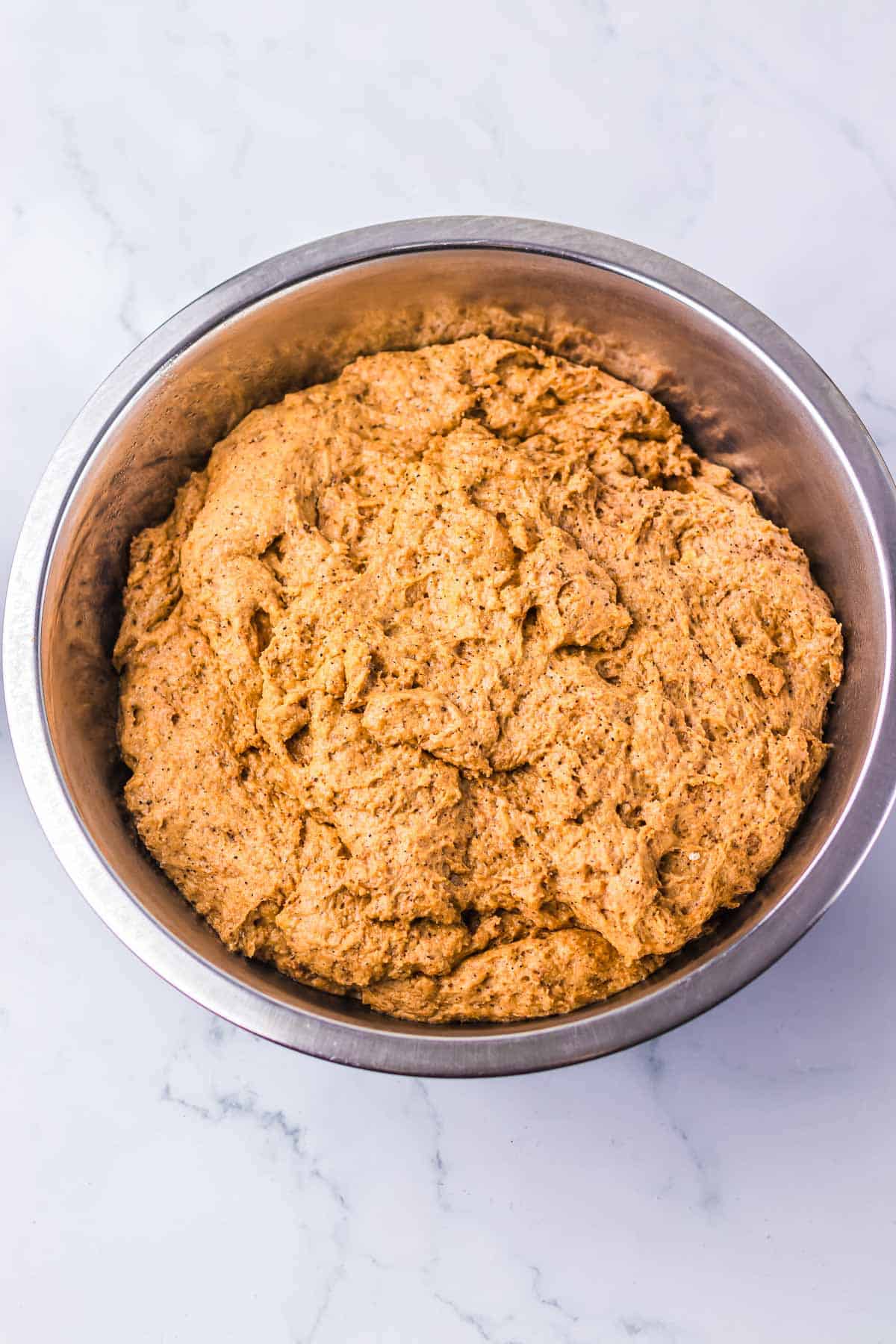 A metal bowl filled with a large amount of Cheesecake Factory Brown Bread dough sits on a marble surface.