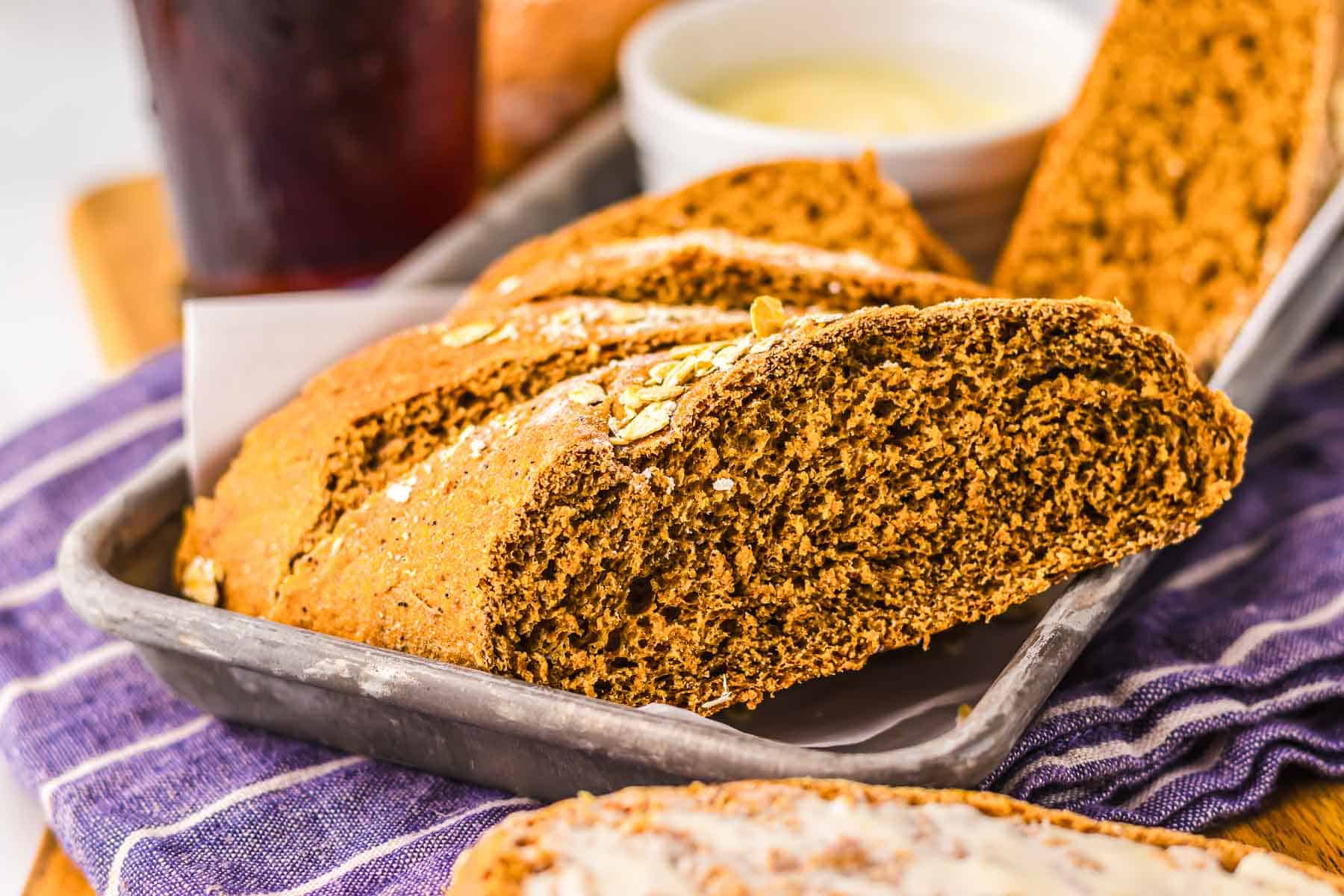 A slice of brown soda bread in a metal tray, with a bowl of butter in the background—just like the classic brown bread served at The Cheesecake Factory.