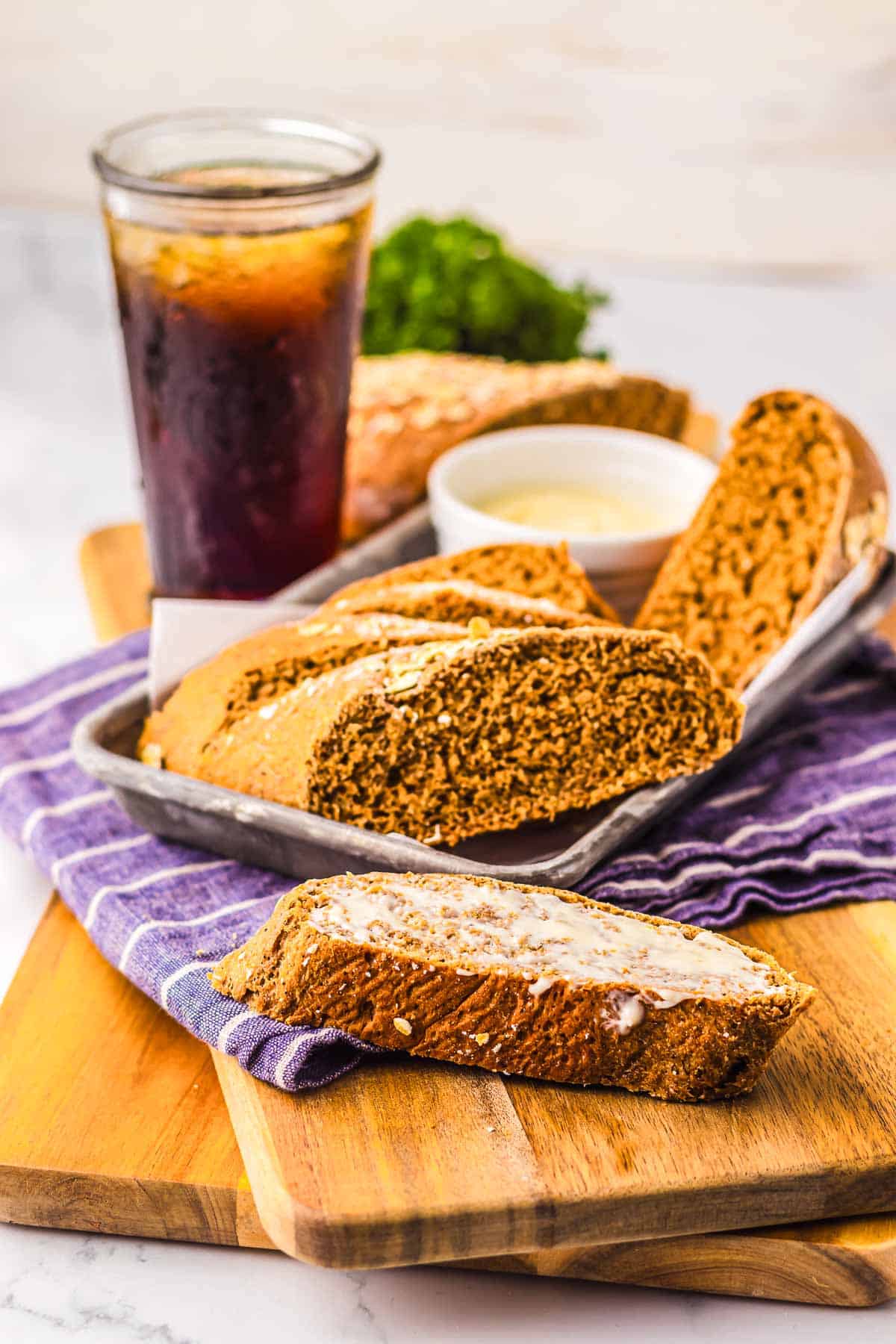 Sliced biscotti with icing on a wooden board, a glass of iced drink, and a small bowl of dip nearby—just like a Cheesecake Factory-inspired treat.