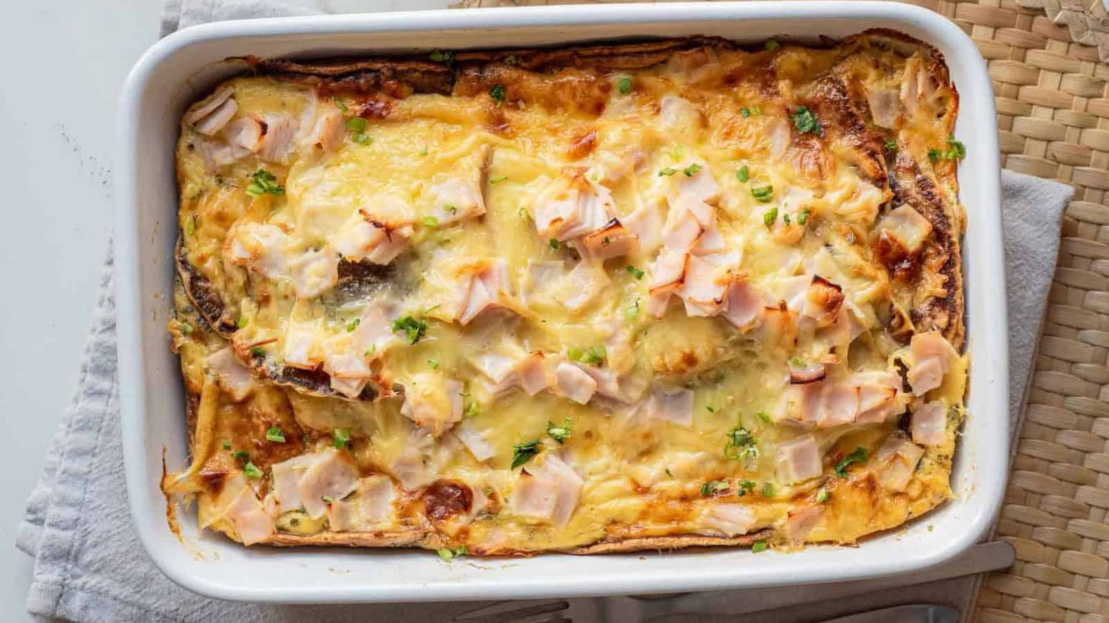 Baked casserole topped with melted cheese and chopped pieces of ham in a white rectangular dish.