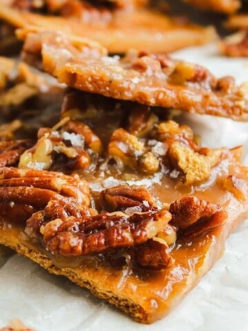 Close-up of pecan toffee bark pieces with caramel and pecans on parchment paper.