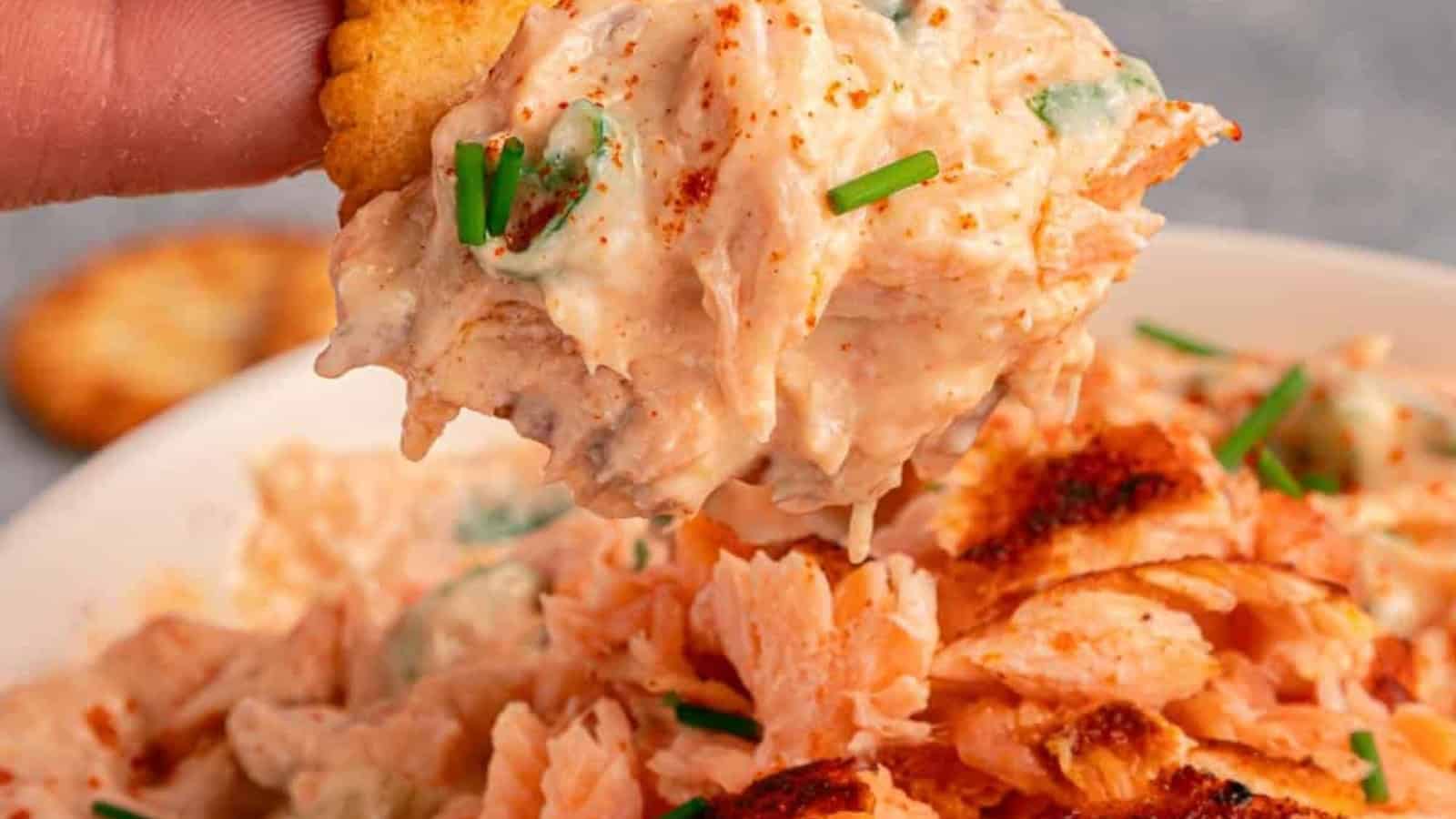 Creamy salmon dip garnished with chives and lemon slices, served with round crackers on the side.