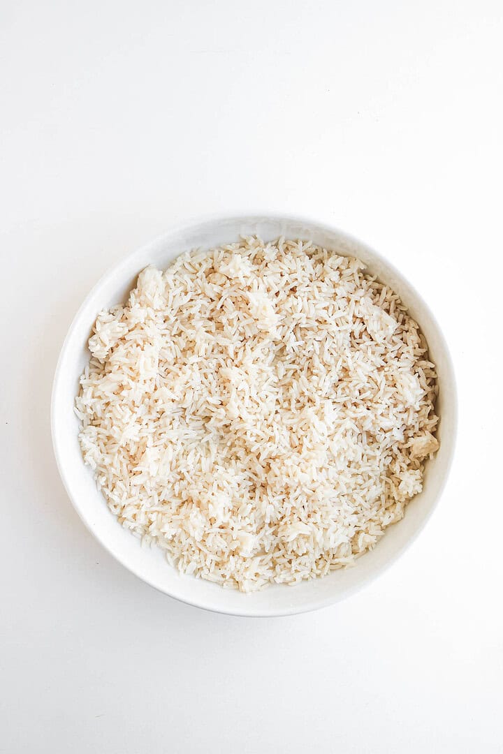 A white bowl filled with uncooked brown rice on a white background, perfect for preparing flavorful Shrimp Fajita Bowls or pairing with a spicy chipotle sauce.