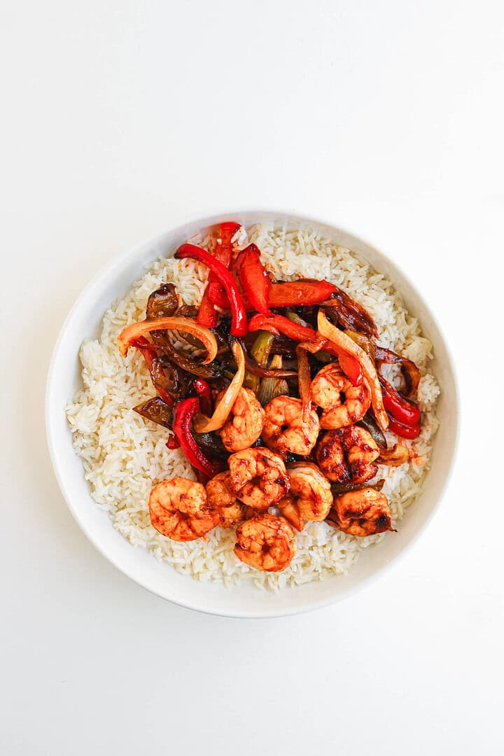 A bowl of white rice topped with shrimp, bell peppers, onions, and chipotle sauce creates delicious Shrimp Fajita Bowls on a white background.