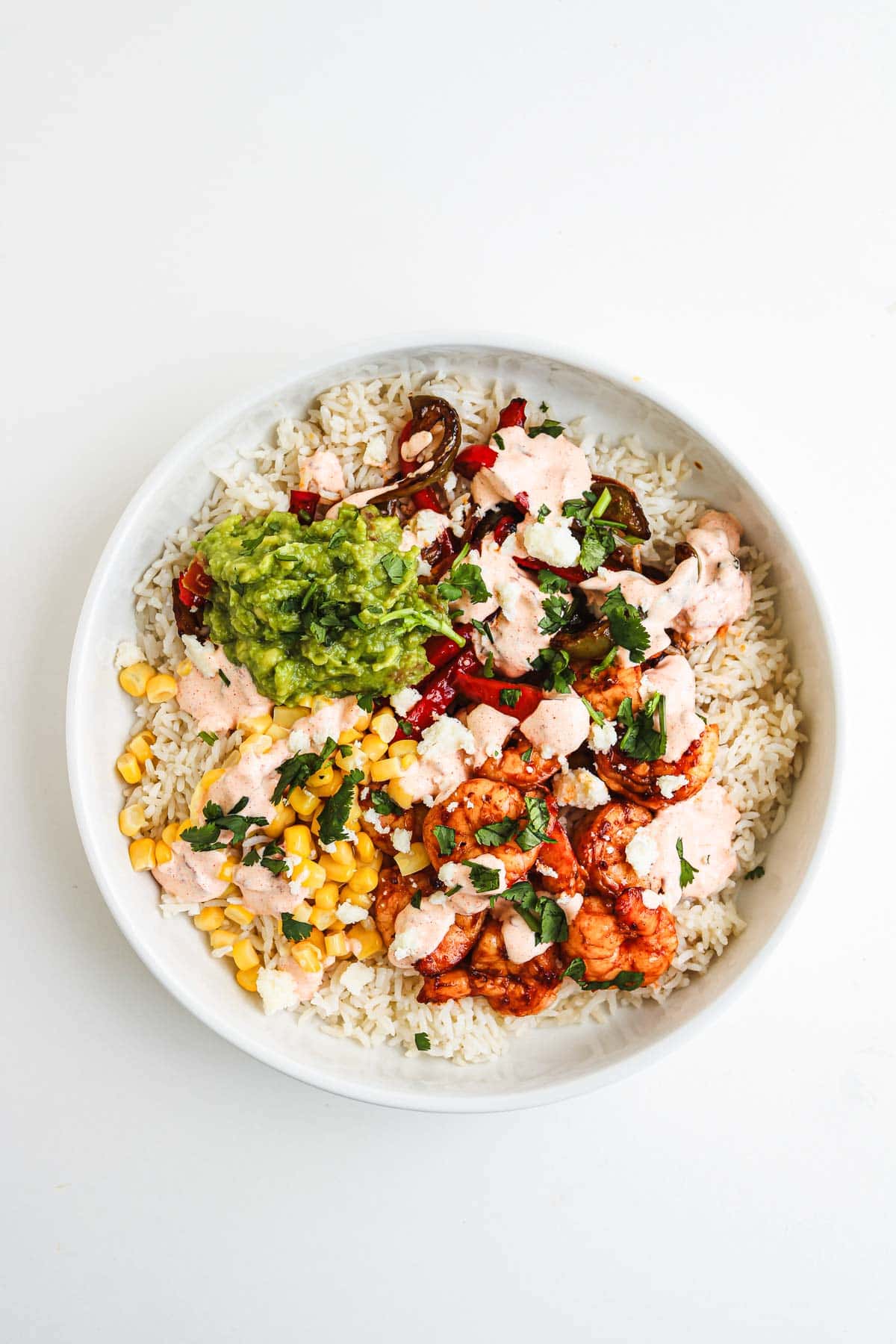 A burrito bowl with rice, corn, guacamole, grilled vegetables, chicken, and a drizzle of Chipotle Sauce on top.
